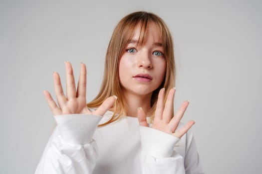 A young woman with long hair expresses surprise and concern against a neutral background in studio