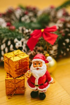 Christmas wreath decorated with pine cones, red bows, and evergreen branches sits on a wooden surface. In front of the wreath, a small Santa Claus figurine and golden ornaments add a cheerful holiday touch