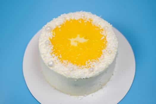 Delicious white cake decorated with orange and coconut flakes standing on white plate on blue background