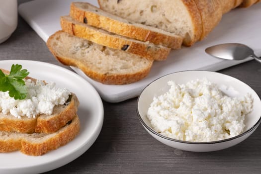 Fresh cottage cheese sits in a bowl beside toasted slices of whole grain bread, creating a comforting meal on a wooden table in a warm kitchen.