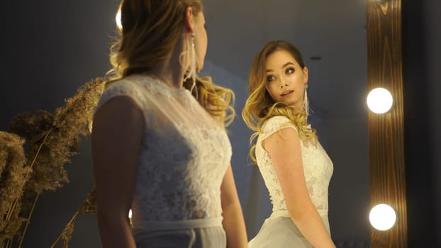 Bride is posing in a white lace dress, looking at her reflection in the mirror