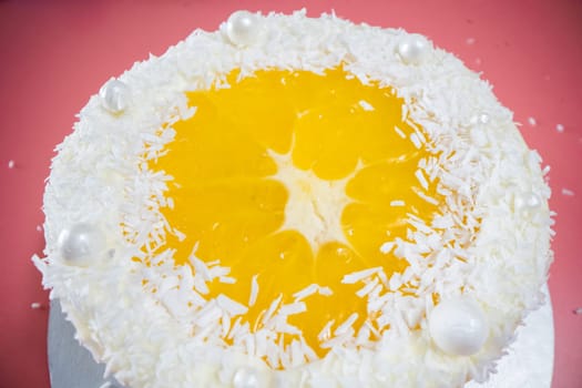 Delicious round cake with coconut shavings and orange jelly decorating the top, creating a joyful and appetizing dessert