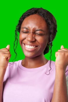 A young woman with braids expresses excitement with a clenched fist against a bright green background in studio