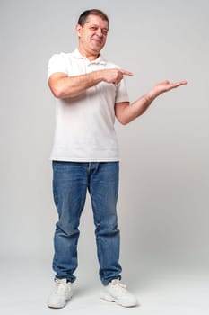 Man dressed in a white polo shirt and jeans happily pointing to the side against a plain background close up