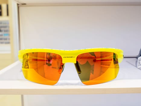 Yellow sport sunglasses with orange mirrored lenses, shown on a white shelf inside a shop, with a shallow depth of field