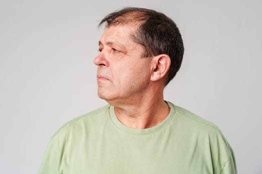 Man in a green shirt gazing thoughtfully to the side in a minimalist setting close up