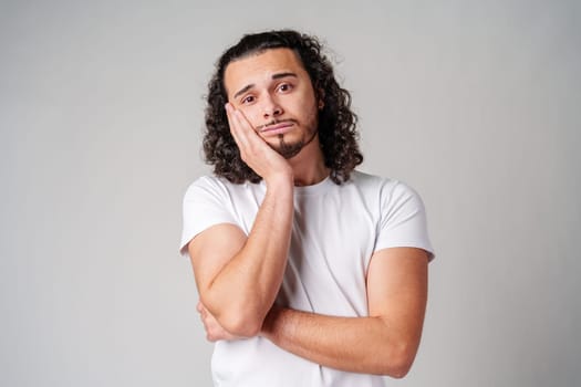 A young man stands thoughtfully against a plain background, expressing contemplation close up
