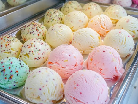 A variety of ice cream scoops in pastel colors, including mint green, pink, and vanilla, are beautifully arranged in a metal tray at a local shop.