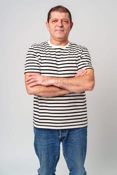 A man stands confidently in a striped shirt, casual jeans with a neutral background in studio