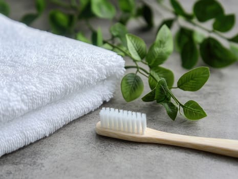 Soft, white towels are neatly arranged beside a bamboo toothbrush and fresh green leaves, highlighting a serene and organized bathroom setting filled with natural elements.