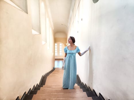 The girl in vintage attire gracefully traverses an ancient castle staircase, embracing the romantic ambiance of her surroundings.
