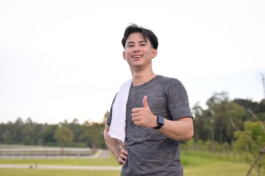 Happy asian man enjoying a morning run in nature and giving a thumbs up. Healthy lifestyle concept.