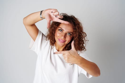 A woman in a white shirt and ripped jeans posing positively with a playful expression in a light studio setting close up