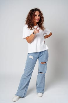 A young woman with curly hair playfully points towards the camera in a bright studio setting