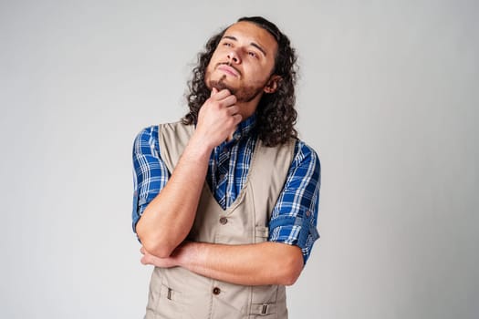 A man with curly hair thoughtfully pondering in a neutral background close up