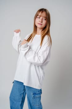 A joyful young girl with long hair wearing a white sweater stands against a plain background close up