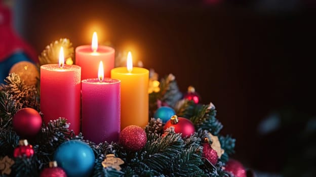 Four lit advent candles are displayed on a christmas wreath with colorful ornaments