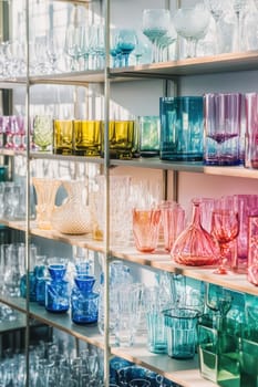 Glassware in a variety of colors and styles are neatly arranged on glass shelves, creating a vibrant and modern display