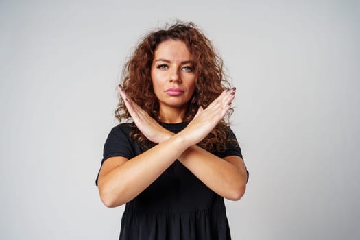 Woman in a black dress standing against a gray background with arms crossed close up