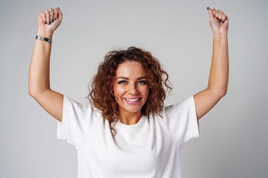 Young woman joyfully celebrates in casual attire against a neutral background close up