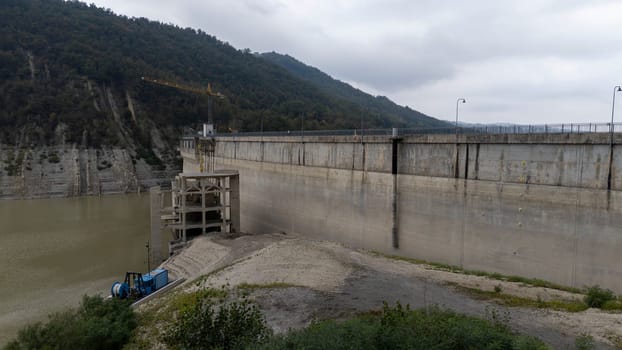 Lago di Mignano, Val Tolla, PC, Italy - October 12nd 2024 Large concrete dam holding back a water reservoir with a construction crane working on a building.