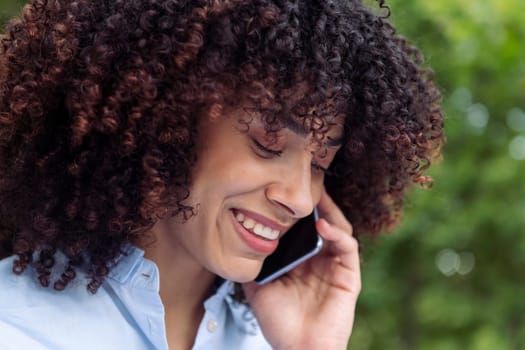 close up portrait of a female entrepreneur with curly hair talking on smart phone at park