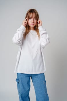 Young girl in a white sweater holding her head in discomfort against a minimalist background close up