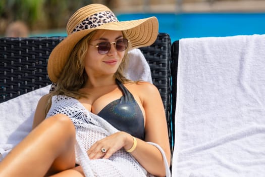 Young woman with glasses and hat lying on chaise longue near pool. Tourism, recreation, relaxation.