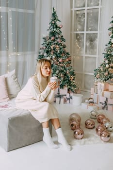 Blonde in a bright Christmas interior with a cup of hot drink with marshmallows. New Year's interior in pink tones. The winter holidays period.