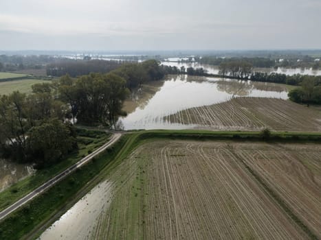 Aerial view of a flooded agricultural landscape with fields and a river overflowing due to heavy rainfall. The flood is causing damage to crops and farmland in Lombardy Italy