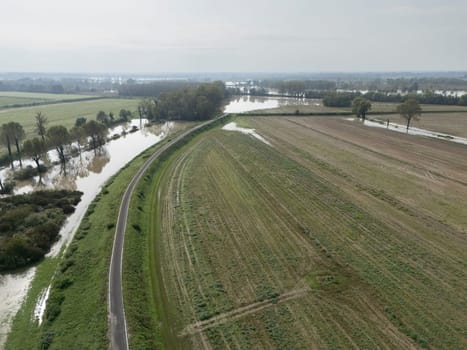 Aerial view of a flooded agricultural landscape with fields and a river overflowing due to heavy rainfall. The flood is causing damage to crops and farmland in Lombardy Italy
