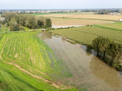 Aerial view of a flooded agricultural landscape with fields and a river overflowing due to heavy rainfall. The flood is causing damage to crops and farmland in Lombardy Italy
