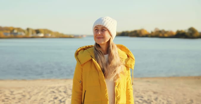 Traveler woman looking away on sunny beach, enjoying amazing landscape, warm weather, wear hat, yellow jacket, standing on sea coast, nature background