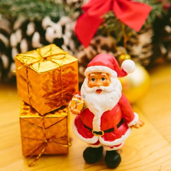 Christmas wreath decorated with pine cones, red bows, and evergreen branches sits on a wooden surface. In front of the wreath, a small Santa Claus figurine and golden ornaments add a cheerful holiday touch