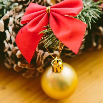 Christmas Decoration. Christmas wreath made of pine cones, decorated with red bows, evergreen branches, and gold ornaments, sits on a wooden surface.