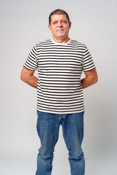 A man stands confidently in a striped shirt, casual jeans with a neutral background in studio