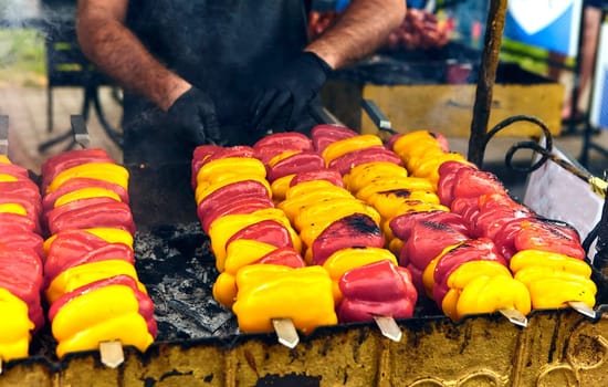 Colorful bell peppers on skewers grilling outdoors, sizzling and charred. A delicious smoky aroma fills the air, creating a vibrant and appetizing scene for a summer barbecue gathering.