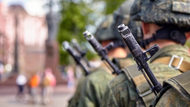 A soldier in full gear stands at attention with a rifle, wearing a helmet and camouflage uniform. Blurred background adds focus and determination to his readiness and vigilance.