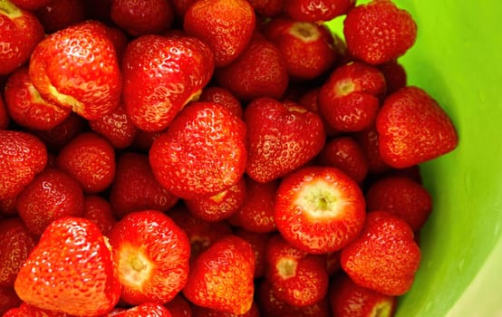 Sun-kissed strawberries, freshly picked and arranged beautifully, sit in a vibrant green bowl, radiating summer's warmth