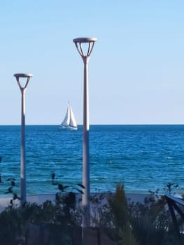 Vertical seascape, street lights on the embankment against the backdrop of the sea horizon and sailboat.