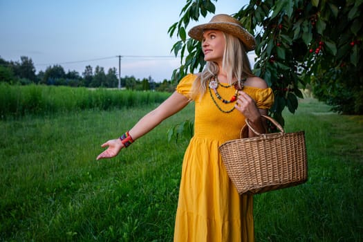 A smiling blonde woman stands near a cherry tree with branches heavy with ripe red cherries. She wears a mustard-colored dress and holds a woven basket, enjoying the sunny spring day.