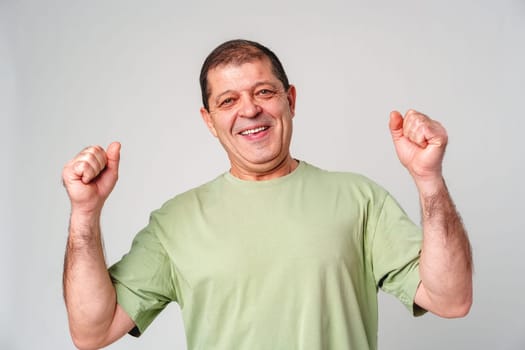 Happy elderly man celebrating a victory with joyful gestures in a light-colored setting close up