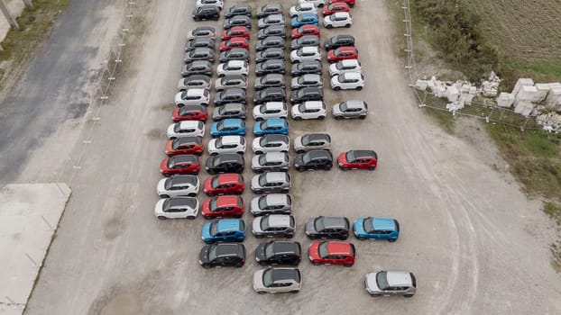 Capturing a busy parking lot from above, shiny new cars await delivery at a distribution center, showcasing the vibrant automotive industry