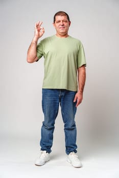 A man with a slight smile making an OK hand gesture against a neutral background close up
