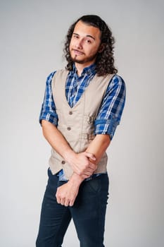 A confident young man with curly hair poses against a neutral backdrop indoors