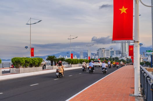 Motorbike traffic on road on a bridge with Vietnam flags in a city in Asia in summer. Nha Trang, Vietnam - August 22, 2024