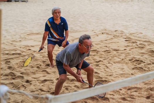 Elderly Asian retired men play badminton on the beach by the sea in summer on vacation in Asia. Nha Trang, Vietnam - September 6, 2024