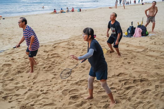 Elderly old Asian retired players play beach badminton with rackets on the beach by the sea in summer on vacation in Asia. Nha Trang, Vietnam - September 6, 2024