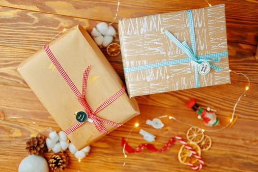 Little tag with Christmas wishes and gifts. Two gift boxes lie on wooden table, on which are attached tags with wishes Happy new year and Holly Jolly