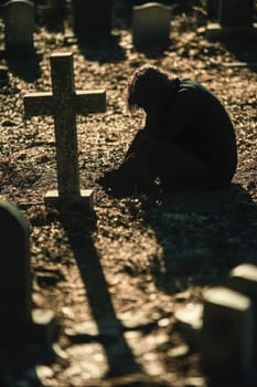 Silhouette of a person grieving at a grave in a cemetery